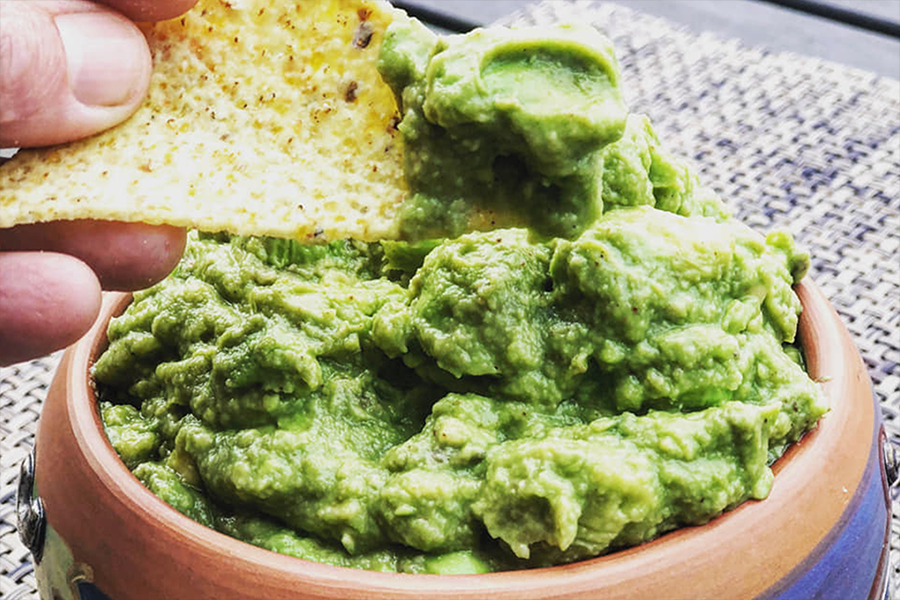 Bowl of Guacamole with someone dipping a tortilla chip in