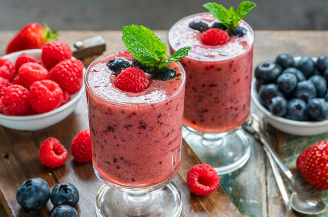 2 glasses of Berry Antioxidant Smoothie with raspberries and blueberries aroud them