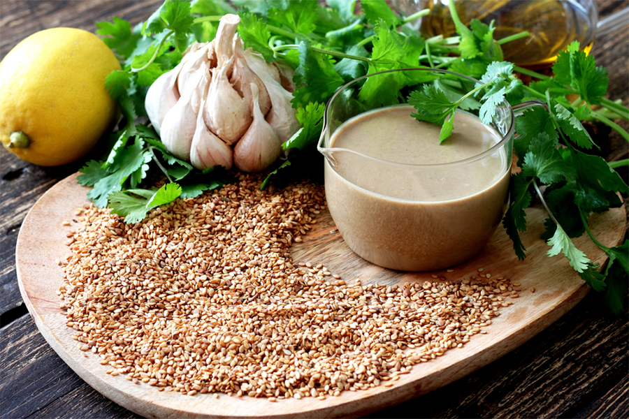 Plate of sesame seeds, a head of garlic, and sauce bowl of tahini sauce