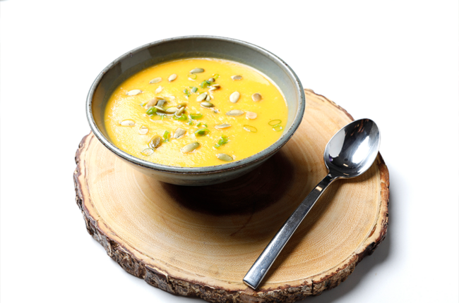 Bowl of Smoky Sweet Potato Soup with Pumpkin Seeds on a tree stump placemat