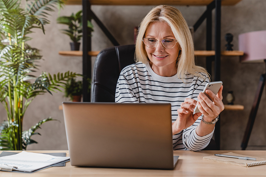 Woman looking at laptop and typing on her phone.