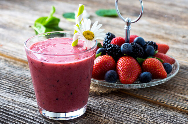 Cup of berry smoothie next to plate of fresh berries
