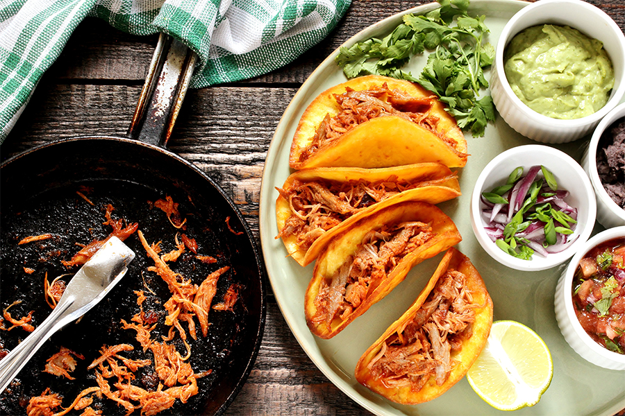 Skillet of shredded chicken and a plate of tacos and toppings
