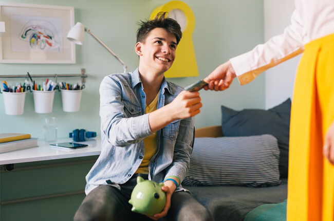 Parent handing teenage son money for piggy bank, teaching about savings