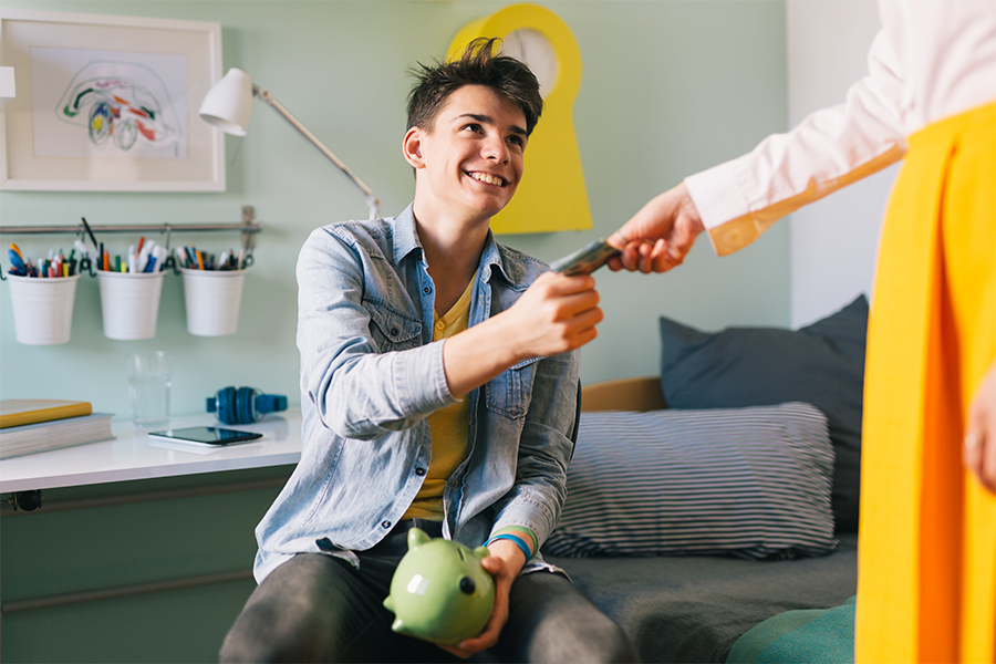 Parent handing teenage son money for piggy bank, teaching about savings