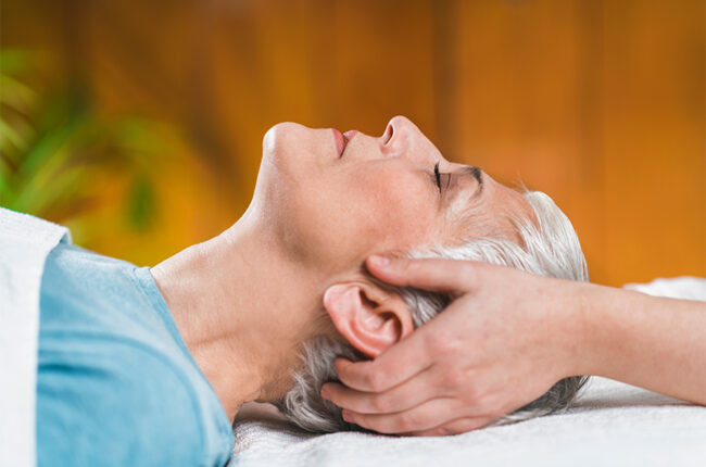 Elderly woman laying on massage chair with woman holding her head