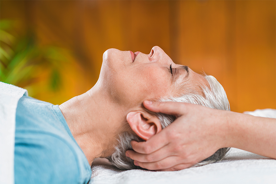 Elderly woman laying on massage chair with woman holding her head
