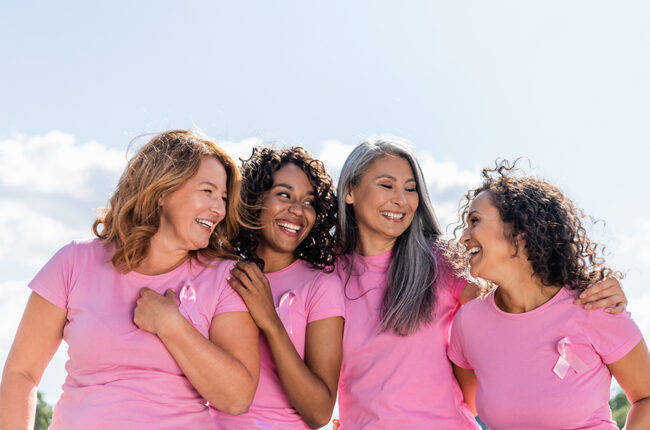 Cheerful multiethnic women with ribbons of breast cancer awareness hugging outdoors