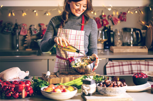 Woman pouring olive oil on a salad in a winter/holiday themed kitchen
