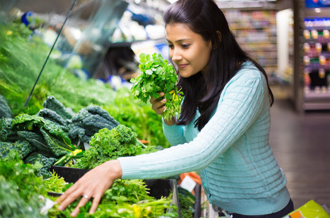 Closeup portrait, beautiful, pretty young woman in sweater picking up, choosing green leafy vegetables in grocery store