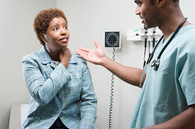 Woman talking to doctor in exam room touching her neck, cancer prevention concept