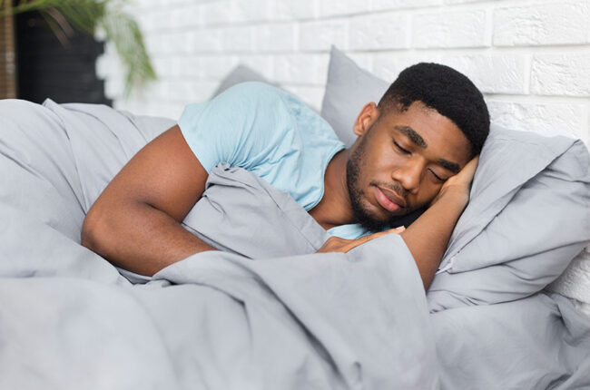 Male sleeping on bed in grey sheets.